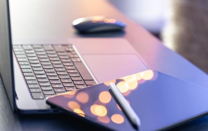 Tablet laying on a desk alongside a laptop and wireless mouse. 