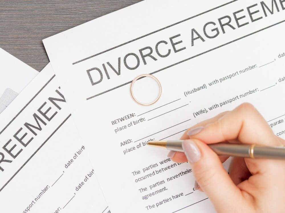 Person signing divorce agreement with a gold wedding ring placed on the document