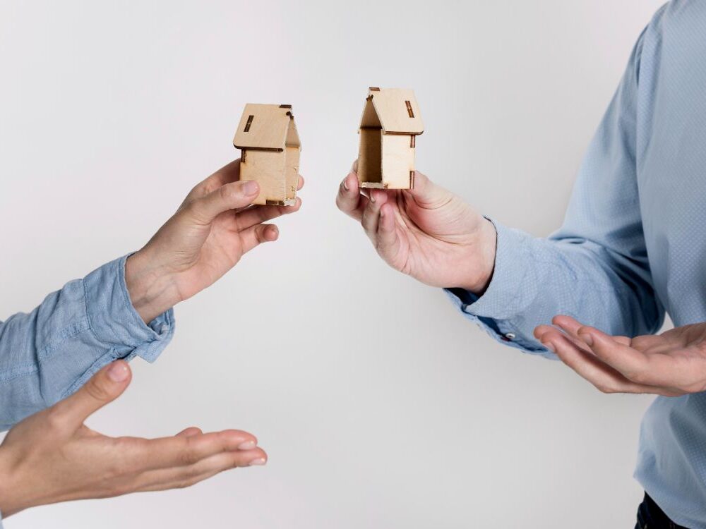 Two people handing over a wooden house model symbolising property transfer during divorce