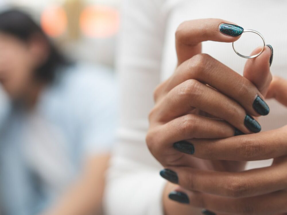 Woman removing wedding ring with blurred partner in background