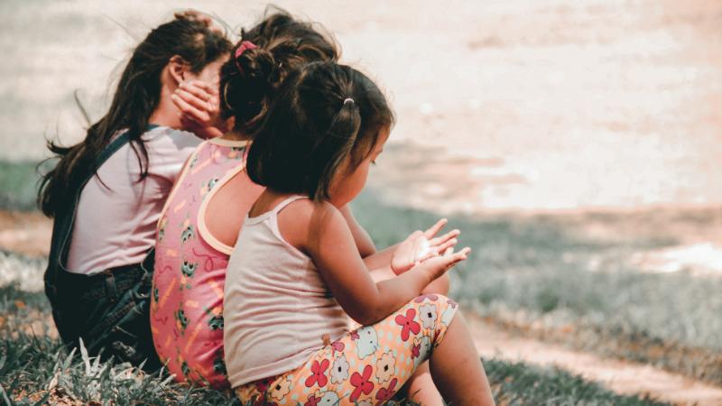 3 children sitting on a path enjoying the sun