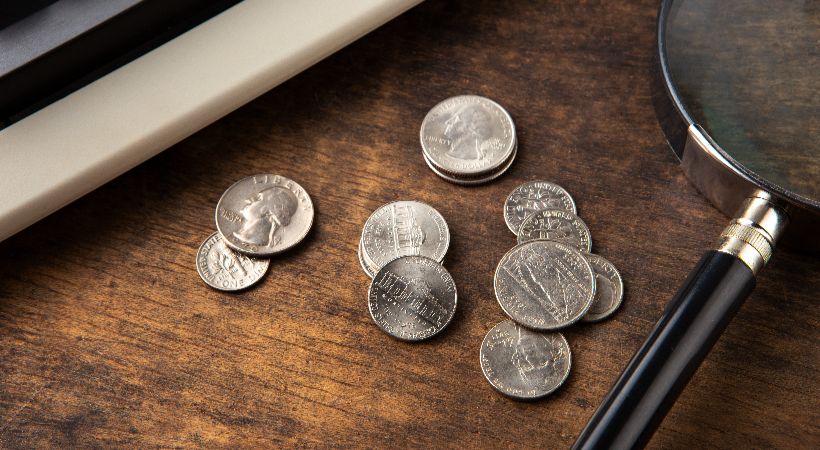Magnifying glass examining coins on a wooden desk.