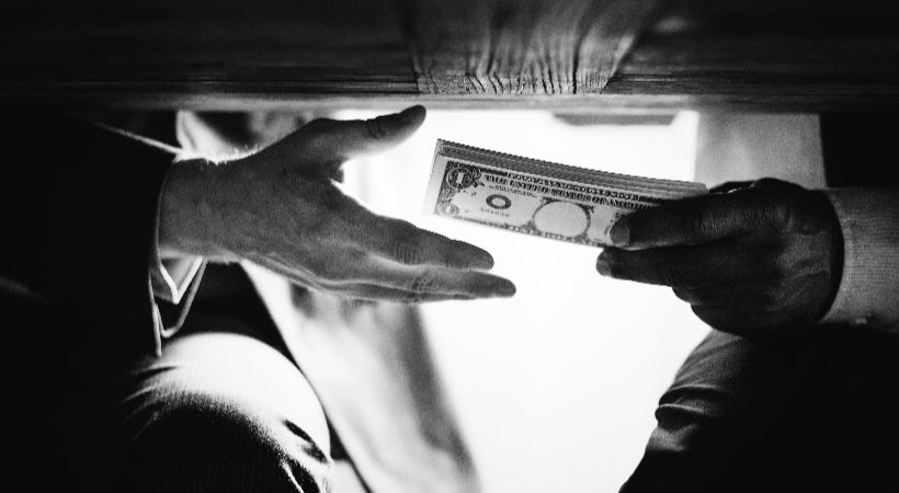 Person exchanging money under a table, representing financial misconduct and economic crime discussed in the Economic Crime and Corporate Transparency Act 2023.