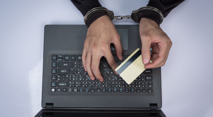 Person in handcuffs holding a credit card over a laptop, symbolising online financial fraud and corporate accountability under the Economic Crime Act 2023.