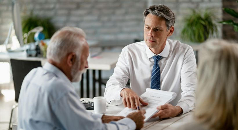 Male solicitor reviewing legal documents with elderly clients in a modern office, representing personal injury case consultation