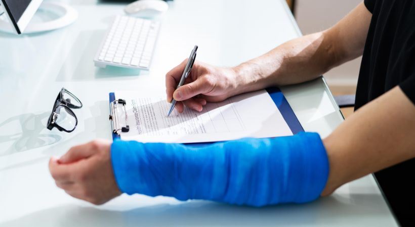 Injured person wearing a blue arm cast signing a legal form at a desk, representing personal injury claim paperwork