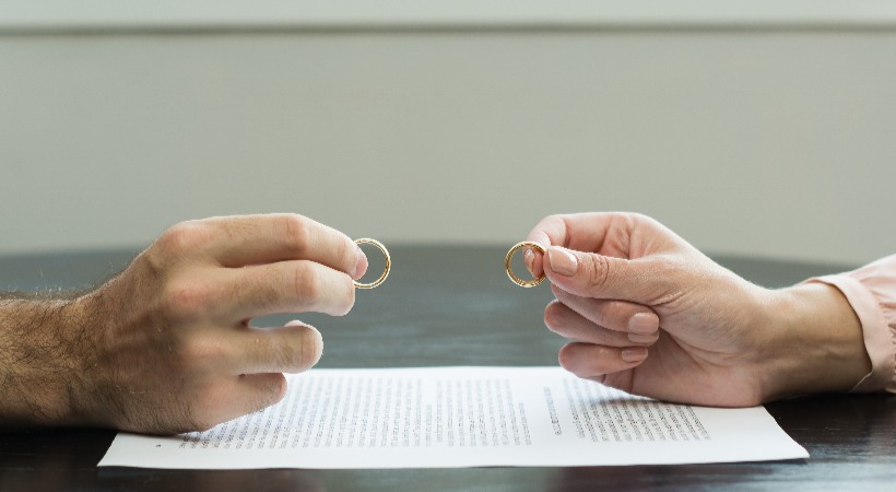Hands of a former couple holding up their wedding rings to another over a divorce agreement document.