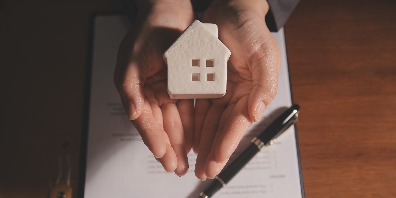 Person holding small home model in their hands over a property agreement document.